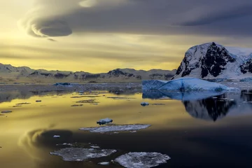 Selbstklebende Fototapeten Antarktis Blue iceberg, mountains and sunset reflecting in ocean at Lemaire Strait, Antarctica  © vadim.nefedov