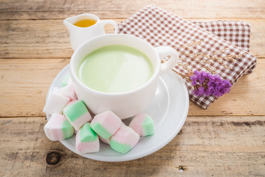 Marshmallows with a cup of green tea milk in white dish on wooden background.