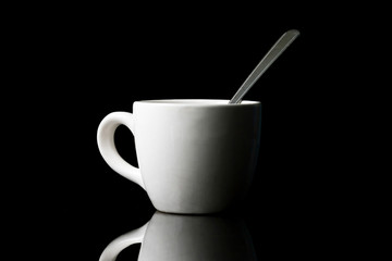 White cup with spoon on black background.