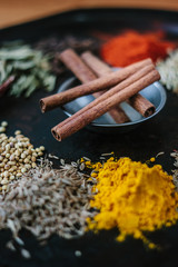 Cinnamon sticks on black metal surface surrounded by spices.