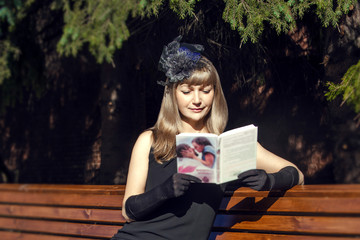 The girl reads the book in the park sitting on a bench.