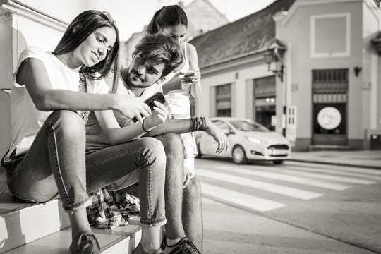 A group of friends sitting on stairs at the street and using smart phones.Sunset .