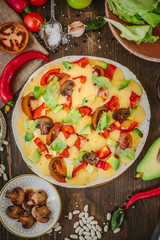Vegetarian home made pizza with mushrooms and vegetables over wooden table, surrounded by ingredients