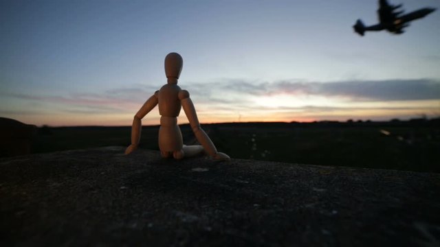 Omino di legno che guarda un aereo al tramonto
