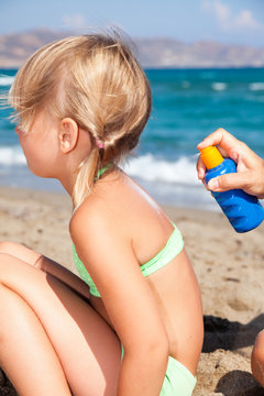 Mother Applying Sunscreen To Her Child At A Beach