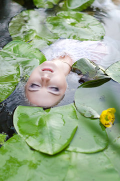 Young woman beauty portrait in water. Girl with gentle makeup in the lake among lotuses and water lilies. Outdoor fashion photo