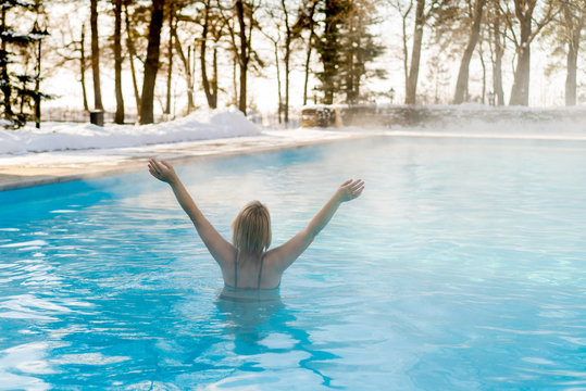 Young blonde woman swimming in outdoors pool at winter day