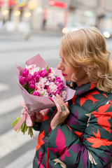 Young blonde woman with flowers bouquet on a city street at cloudy day
