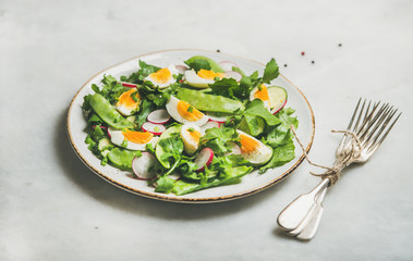 Healthy spring green salad with radish, boiled egg, arugula, green pea and mint in white plate over grey marble background, selective focus, horizontal composition
