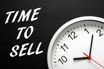 The words Time To Sell in white text on a blackboard next to a modern wall clock as a reminder