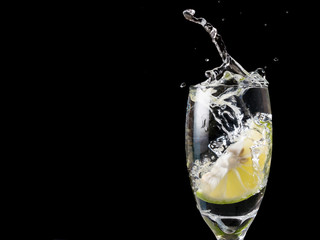 Glass of water with lime on black background.