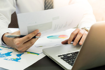 Close up of Businessman analyzing investment charts and using laptop on the desk.