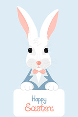 A white rabbit with pink ears in a blue jacket with a bow holds in his paws a card with the hand written Happy Easter