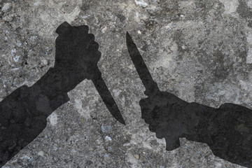 Two human hands with knives silhouette in shadow on concrete wall background, with space for text or image.