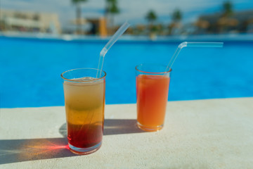 Glasses with tasty cocktail in front of a swimming pool with clear water. Close-up photo. Palm trees on the background. Vacation at a resort in summer