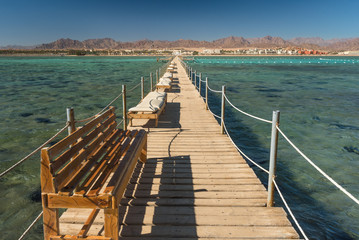 Pier with chaise longues in the sea in resort. Summer vacation. View at a clear sea with turquoise water. Summer vacation at a sea coastline in a exotic country.