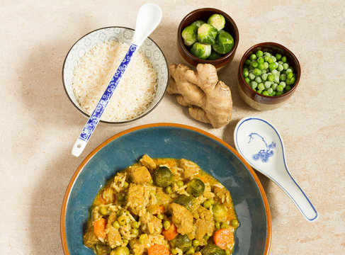 Curry with pork, brussels sprouts and green peas. Blue plate, rice, ginger, green peas.