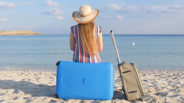 Young woman traveler sits on the beach with a suitcase