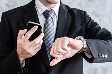 Close up of businessman using smart phone and checking time on his wrist watch.