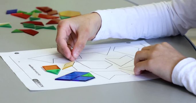 Close up shot of a child using plastic geometric shapes to fill in the outline of a shape on a piece of paper