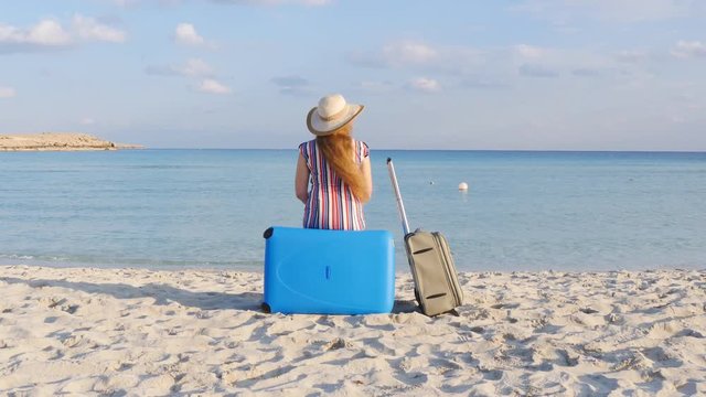 Young woman traveler sits on the beach with a suitcase