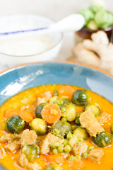 Curry with pork, brussels sprouts and green peas. Blue plate, rice, ginger, green peas.