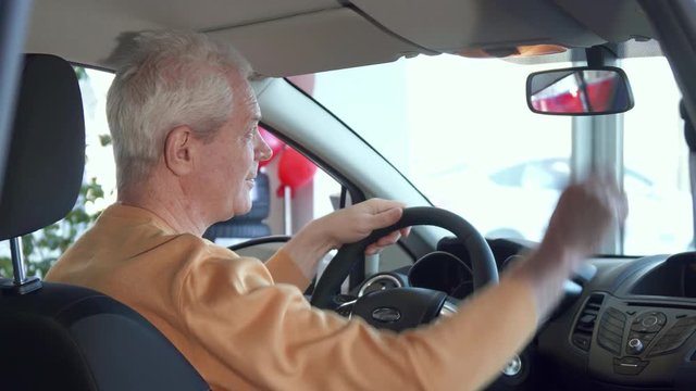 Senior caucasian man adjusting rear-view mirror inside the car. Aged male customer smiling for the camera. Attractive gray client approving the interior of the vehicle