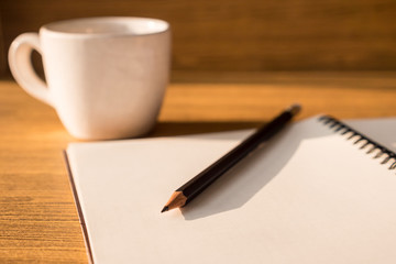 Blank notebook with pencil and coffee cup on wooden table background. Selective focus