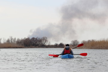 Man with girl rowing in blue kayak on cloudy calm winter day on river with dry bulrush and trees. Winter kayaking. Sports and recreation.