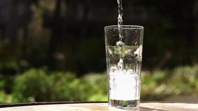 Pouring water into glass placed on table. Container being filled with drinking water. Slow motion full HD video footage 1920x1080