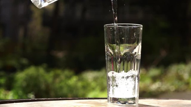 Pouring water into glass placed on table. Container being filled with drinking water. Slow motion full HD video footage 1920x1080
