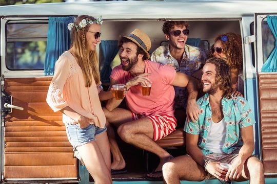 Group of happy friends sitting in campervan and drinking beer
