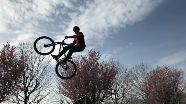 Boy riding a bike performing a trick in silhouette against sunset sky, in slow motion.