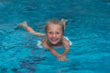 Fototapeta na wymiar Little girl learning to swim in big sport pool. Swimming school for small children. Healthy kid enjoying active lifestyle. Preschooler practicing with foam pad.