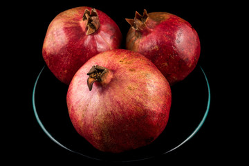 Three pomegranates on plate with black background