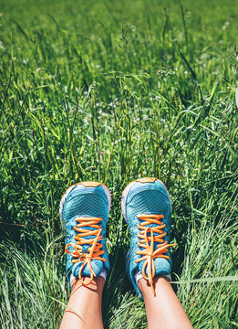 Woman feet in bright blue running shoes are in high green grass