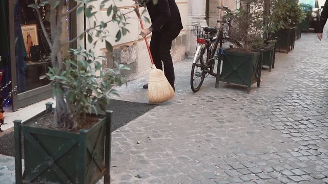 The man the janitor cleans street. Owners of shop prepares for opening, works with broom. Slow motion.