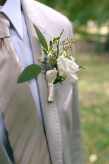 Boutonniere of white and yellow flowers with greens on lapel of a gray jacket