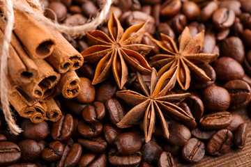 Coffee beans and cinnamon on a background of burlap. Roasted coffee beans background close up. Coffee beans pile from top with copy space for text. Seasoning. Spice. Cinnamon. Badian. Coffee house.