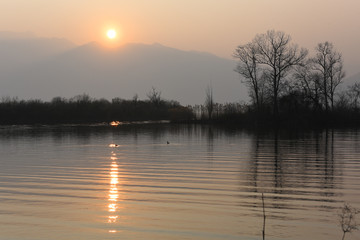 Tramonto del sole sul lago in una sera di primavera, con riflessi arancioni rosati