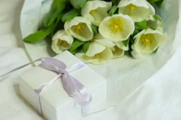 Gift box and a bouquet of white tulips on a bed. Holidays. Spring.