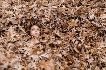 Child under pile of leaves with face exposed