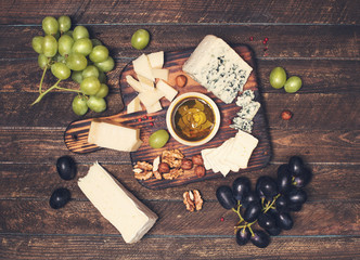 Cheese plate: Emmental, brie cheese, blue cheese, walnuts, hazelnuts, honey, grapes on wooden table