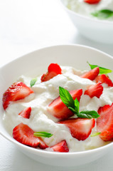 Breakfast with bowl of thick organic greek yogurt and fresh strawberries on white backgfound