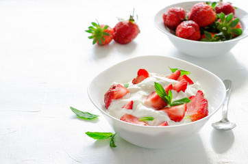 Breakfast with bowl of thick organic greek yogurt and fresh strawberries on white backgfound