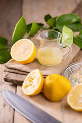 glass bowl of freshly squeezed lemon juice, lemon squeezer and ripe lemons on wooden background