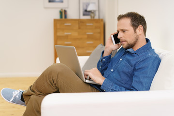 mann sitzt auf dem sofa mit laptop und handy