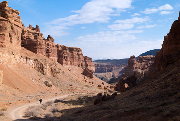 Fototapeta premium Sharyn Canyon panorama. View of the Valley of Castles in the Sharyn Canyon National Park, Kazakhstan. Distant hikers are walking along the road. Early spring sunny day.
