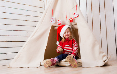 pretty little girl in red santa hat sitting near wigwam with toy-ball in hand © Ievgen Skrypko