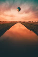 Fototapete Dunkelbraun Bunter Heißluftballon, der bei Sonnenuntergang über einen kleinen Fluss auf dem Land fährt.